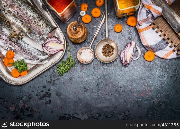 Raw fish fillets with cut vegetables, herbs and spices for tasty seafood dish cooking, preparation on dark rustic background, top view, border