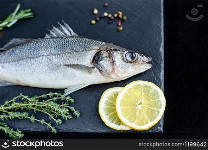 Raw fish sea bass with spices and herbs on black slate table. Fresh sea bass. Top view with copy space.. Fresh sea bass. Raw fish sea bass with spices and herbs on black slate table.