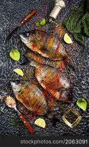 Raw fish with herbs, lemon and olive oil on dark textured background.