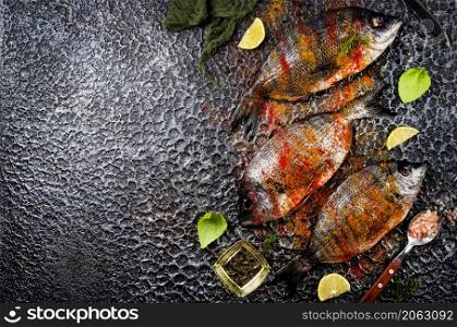Raw fish with herbs, lemon and olive oil on dark textured background.