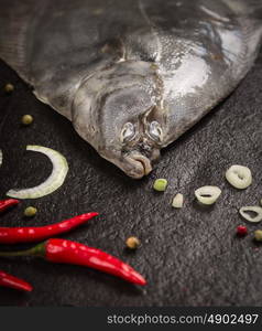 raw flounder head with spices on dark stone background