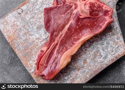 Raw fresh juicy beef t-bone steak with salt, spices and herbs on a dark concrete background