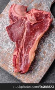 Raw fresh juicy beef t-bone steak with salt, spices and herbs on a dark concrete background