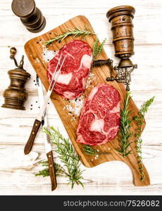 Raw fresh meat Rib Eye Steak with herbs on wooden background. Fork and knife for food preparation