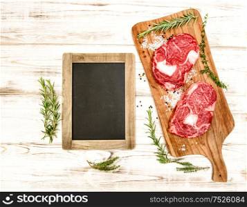 Raw fresh meat with herbs, spices and blackboard on wooden desk. Food background