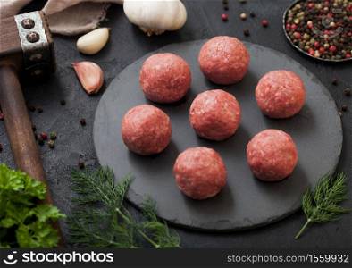 Raw fresh minced beef meatballs on round board with pepper,garlic and parsley on black table background.