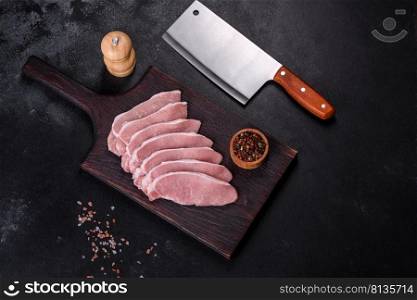 Raw fresh pork meat sliced on a wooden cutting board against a dark concrete background. Raw fresh pork meat sliced on a wooden cutting board