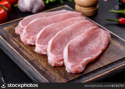 Raw fresh pork meat sliced on a wooden cutting board against a dark concrete background. Raw fresh pork meat sliced on a wooden cutting board