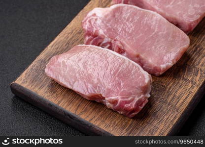 Raw fresh pork meat steak with salt, spices and herbs on a wooden cutting board