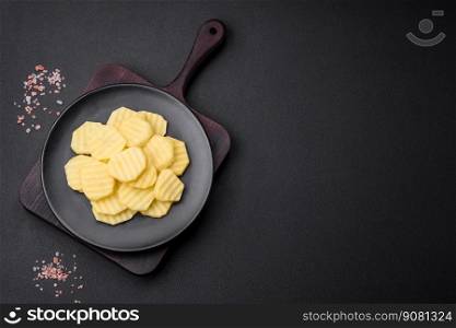 Raw fresh potatoes cut into slices on a black ceramic plate on a dark concrete background