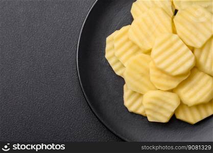Raw fresh potatoes cut into slices on a black ceramic plate on a dark concrete background