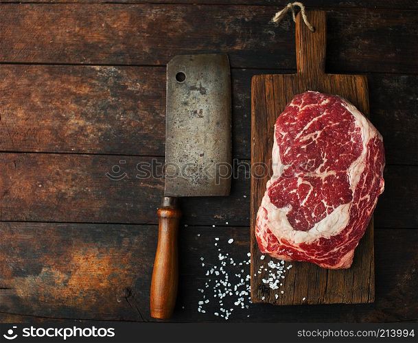 Raw fresh ribeye steak with salt and an ax on a wooden background