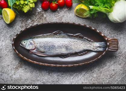 Raw fresh whole trout in baking dish with vegetables cooking ingredients on gray concrete background , top view. Healthy Food concept