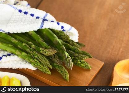 Raw green asparagus wrapped in a dish towel lying on a wooden board (Selective Focus, Focus on the asparagus heads in the front). Raw Green Asparagus