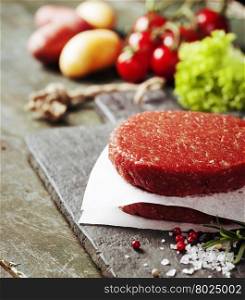 Raw Ground beef meat Burger steak cutlets with seasoning and vegetables on vintage wooden boards
