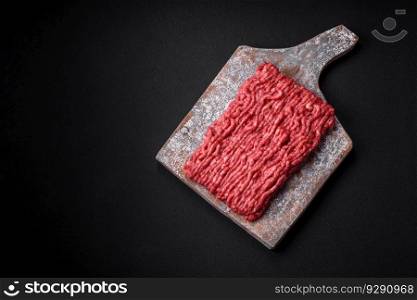 Raw ground beef or pork on a wooden cutting board with spices and salt on a dark concrete background