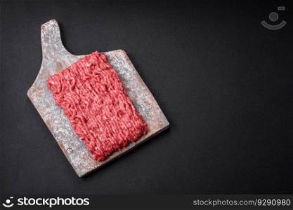 Raw ground beef or pork on a wooden cutting board with spices and salt on a dark concrete background
