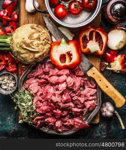 Raw gut meat with kitchen knife fresh vegetables, seasoning and spices for tasty cooking on dark rustic background, top view