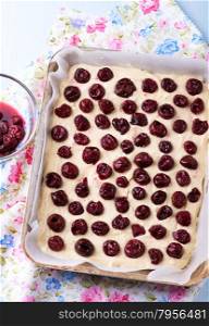 Raw homemade cherry cake in baking tray ready for oven, top view
