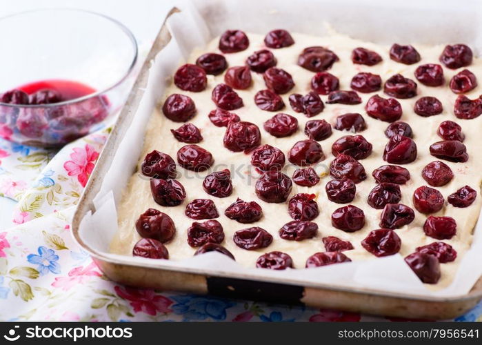 Raw homemade cherry cake in baking tray ready for oven, top view