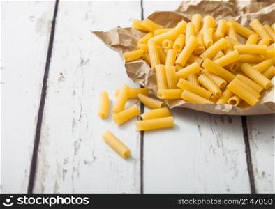 Raw homemade penne pasta in brown paper on white wooden background. Macro