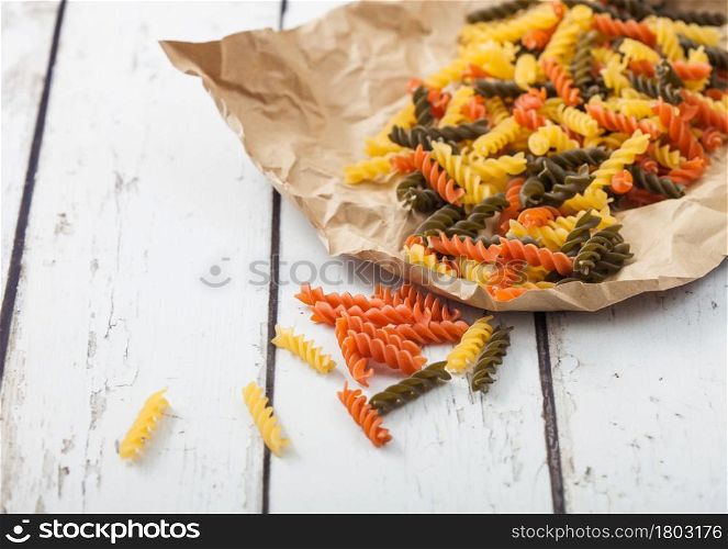 Raw homemade tricolore fusilli pasta in brown paper on white wooden table background.