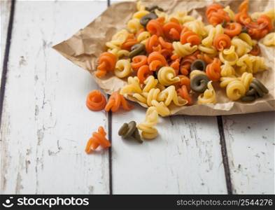 Raw homemade tricolore trottole pasta in brown paper on white.