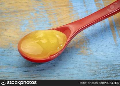 raw honey on a red stoneware teaspoon against grunge rustic wood
