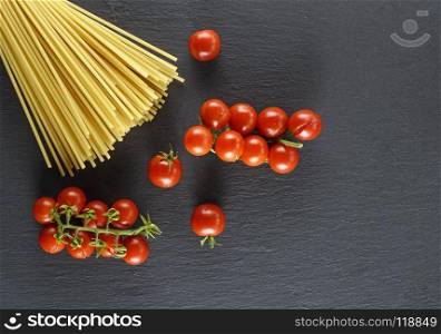 raw Italian long pasta and ripe red cherry tomatoes on a black background, copy space