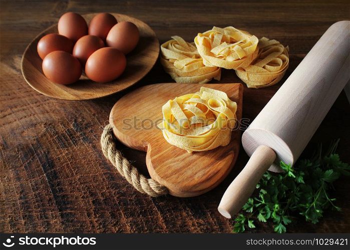 Raw italian pasta tagliatelle on wooden board and rolling pin on rustic background. Selective focus .. Raw italian pasta tagliatelle on wooden board and rolling pin on rustic background. Selective focus