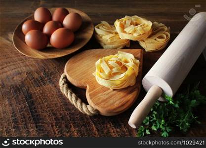 Raw italian pasta tagliatelle on wooden board and rolling pin on rustic background. Selective focus .. Raw italian pasta tagliatelle on wooden board and rolling pin on rustic background. Selective focus