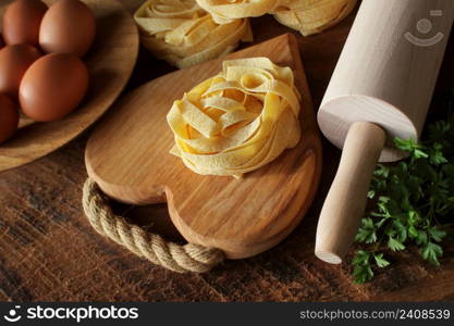 Raw italian pasta tagliatelle on wooden board and rolling pin on rustic background. Selective focus .. Raw italian pasta tagliatelle on wooden board and rolling pin on rustic background. Selective focus