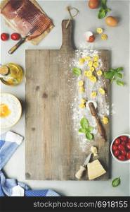 raw italian pasta tortellini with ingredients on wooden board. Top view
