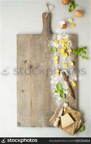 raw italian pasta tortellini with ingredients on wooden board. Top view