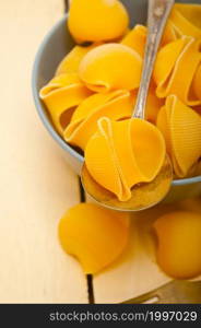 raw Italian snail lumaconi pasta on a blue bowl over rustic table macro