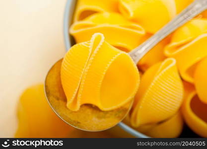 raw Italian snail lumaconi pasta on a blue bowl over rustic table macro