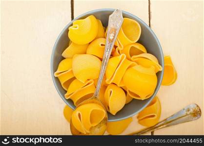 raw Italian snail lumaconi pasta on a blue bowl over rustic table macro