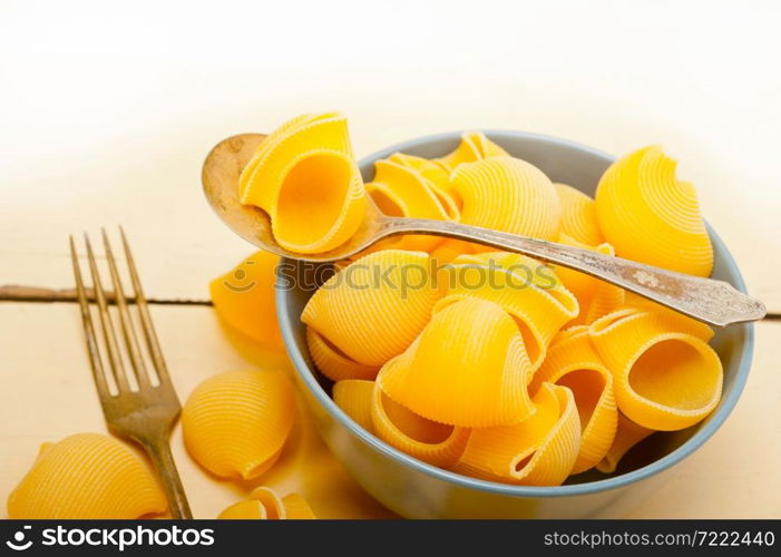 raw Italian snail lumaconi pasta on a blue bowl over rustic table macro