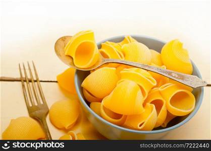 raw Italian snail lumaconi pasta on a blue bowl over rustic table macro