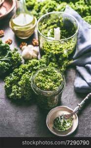 Raw kale eating recipes. Green kale pesto in glass on dark rustic kitchen table background with ingredients, top view. Kale preparation. Healthy detox vegetables . Clean eating and dieting concept.