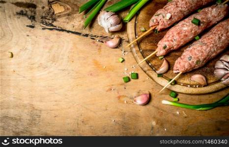 Raw kebab of beef with garlic and onions. On a wooden table.. Raw kebab of beef with garlic and onions.