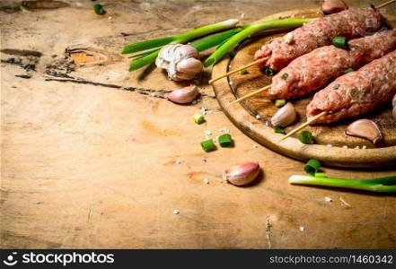 Raw kebab of beef with garlic and onions. On a wooden table.. Raw kebab of beef with garlic and onions.