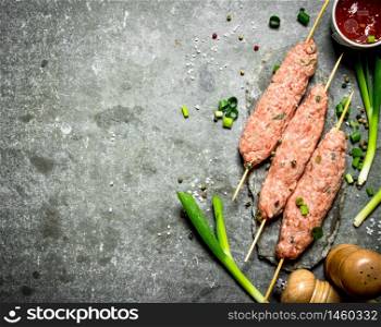 Raw kebab with green onions and tomato sauce. On the stone table.. Raw kebab with green onions and tomato sauce.