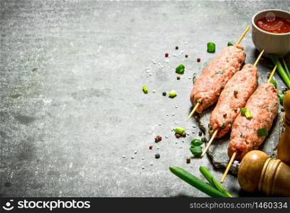 Raw kebab with green onions and tomato sauce. On the stone table.. Raw kebab with green onions and tomato sauce.