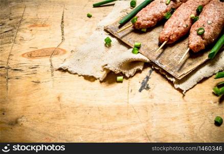 Raw kebab with green onions on the Board. On a wooden table.. Raw kebab with green onions on the Board.