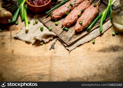 Raw kebab with tomato sauce and green onions. On a wooden table.. Raw kebab with tomato sauce and green onions.