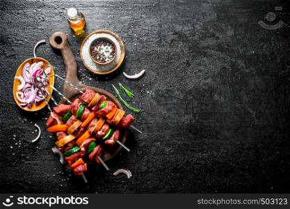 Raw kebab with vegetables, spices, oil and cut onion in bowl. On black rustic background. Raw kebab with vegetables, spices, oil and cut onion in bowl.