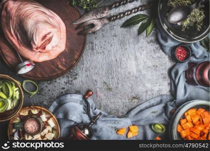 Raw Knuckle eisbein cooking preparation on dark rustic background with herbs, spices and cut vegetables ingredients in bowls, top view, frame