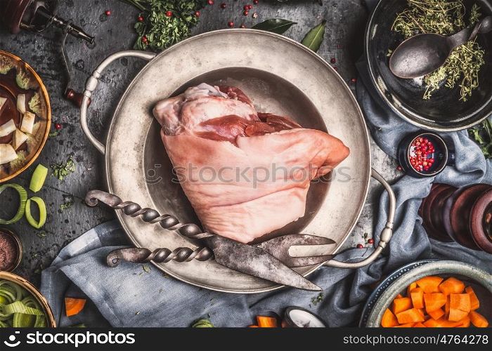 Raw Knuckle eisbein in vintage bowl with rustic meat fork and knife , preparation with cooking ingredients, top view