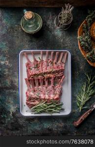 Raw lamb ribs with herbs and seasonings on a dark rustic kitchen background. Seasonings and spices are lined around. Top view.